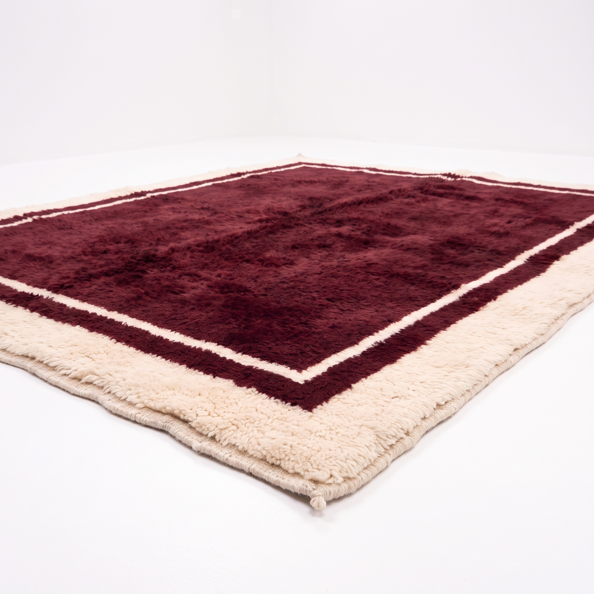 Burgundy hand-knotted Moroccan shag rug with cream border, angled view showing the plush wool pile