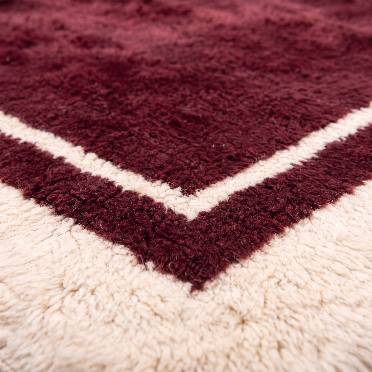 Close-up of the carved cream border and thin inner line on a burgundy Beni Mrirt wool rug