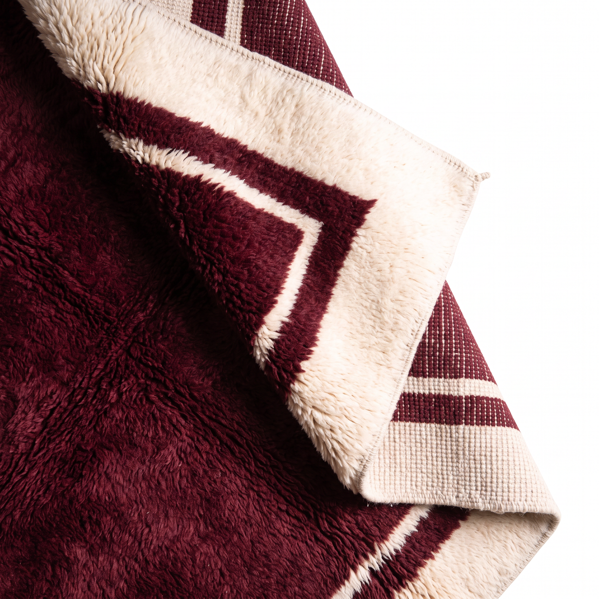 Corner of a burgundy Moroccan rug lifted to show the shaggy wool pile on the front and the flat hand-knotted back