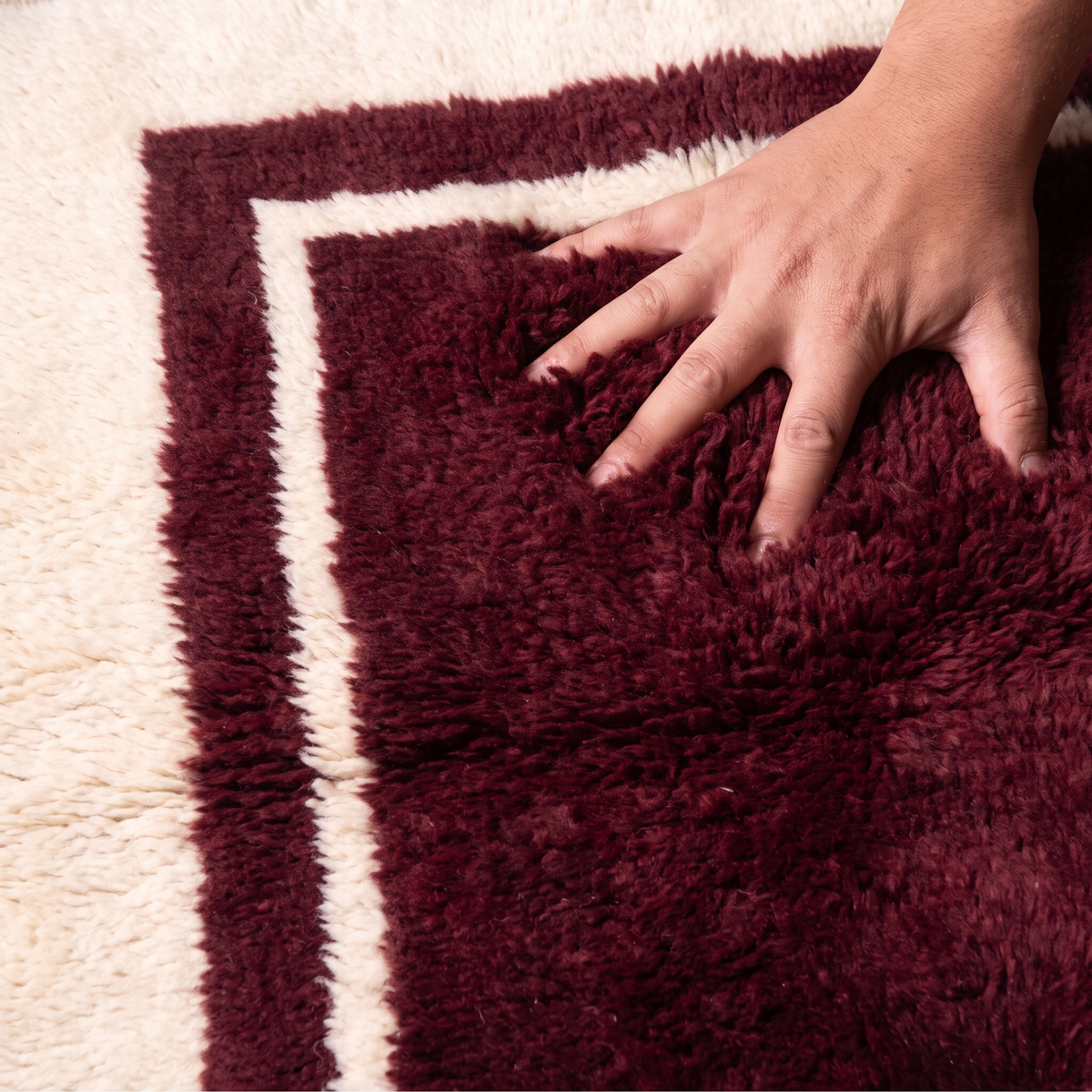 Hand pressing into the deep plush pile of a burgundy hand-knotted wool rug