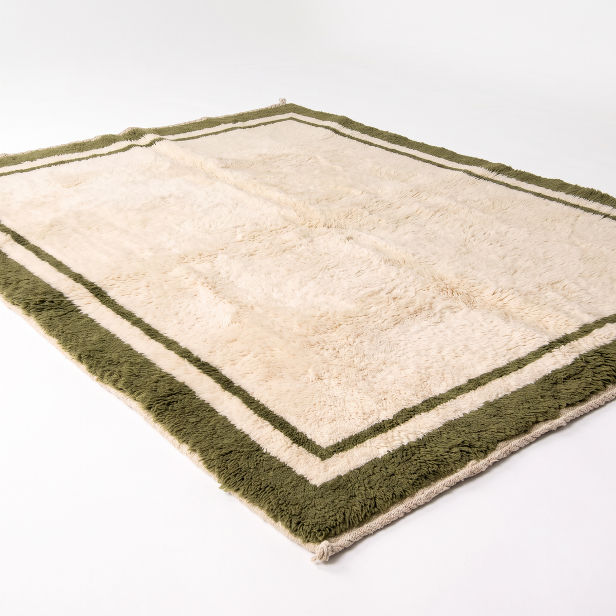 Cream hand-knotted Moroccan shag rug with olive green border, angled view showing the plush wool pile